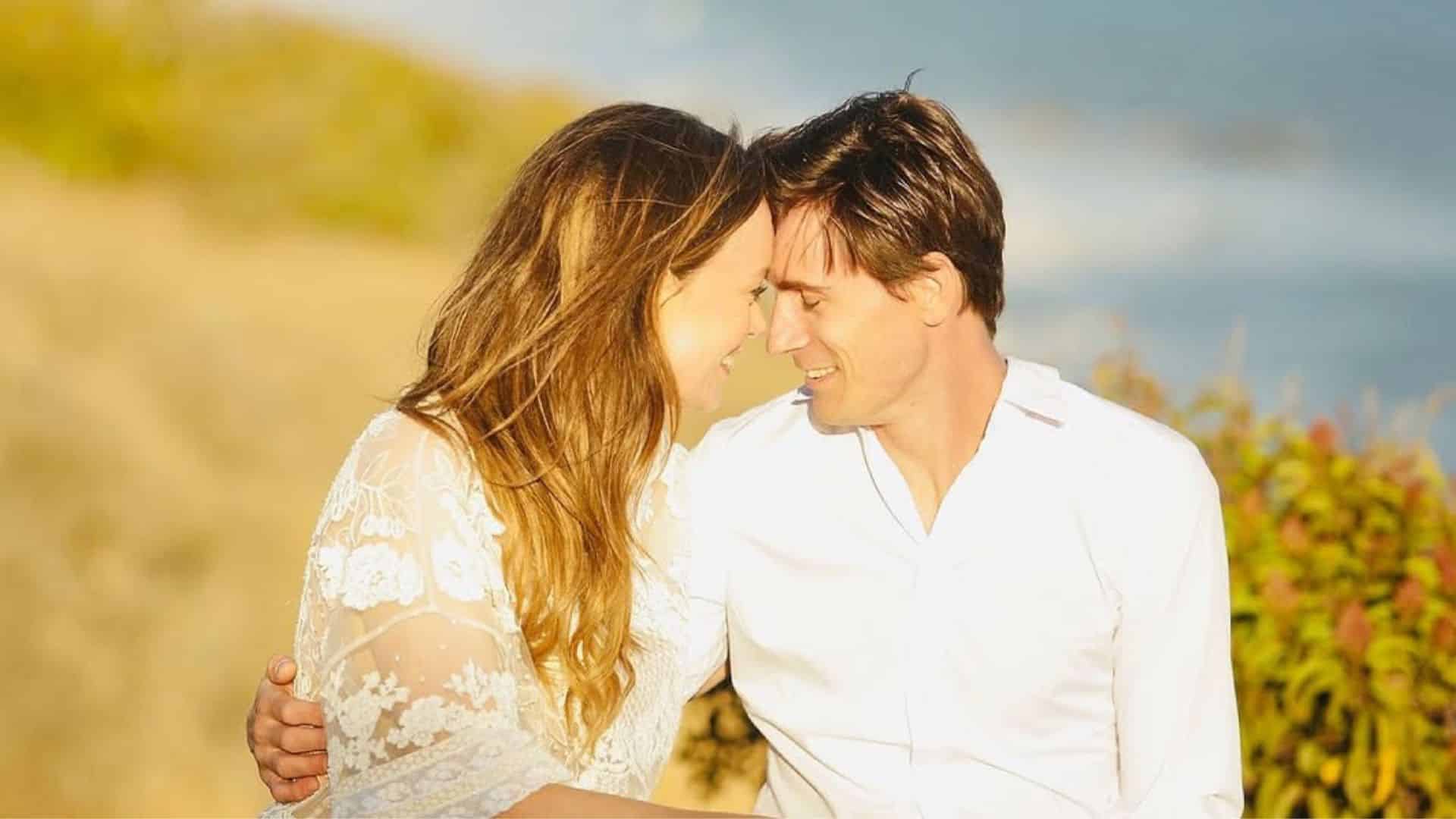 Tolya Ashe and Rachel Boston sitting close together outdoors, smiling and leaning forehead to forehead in a warm, sunlit setting