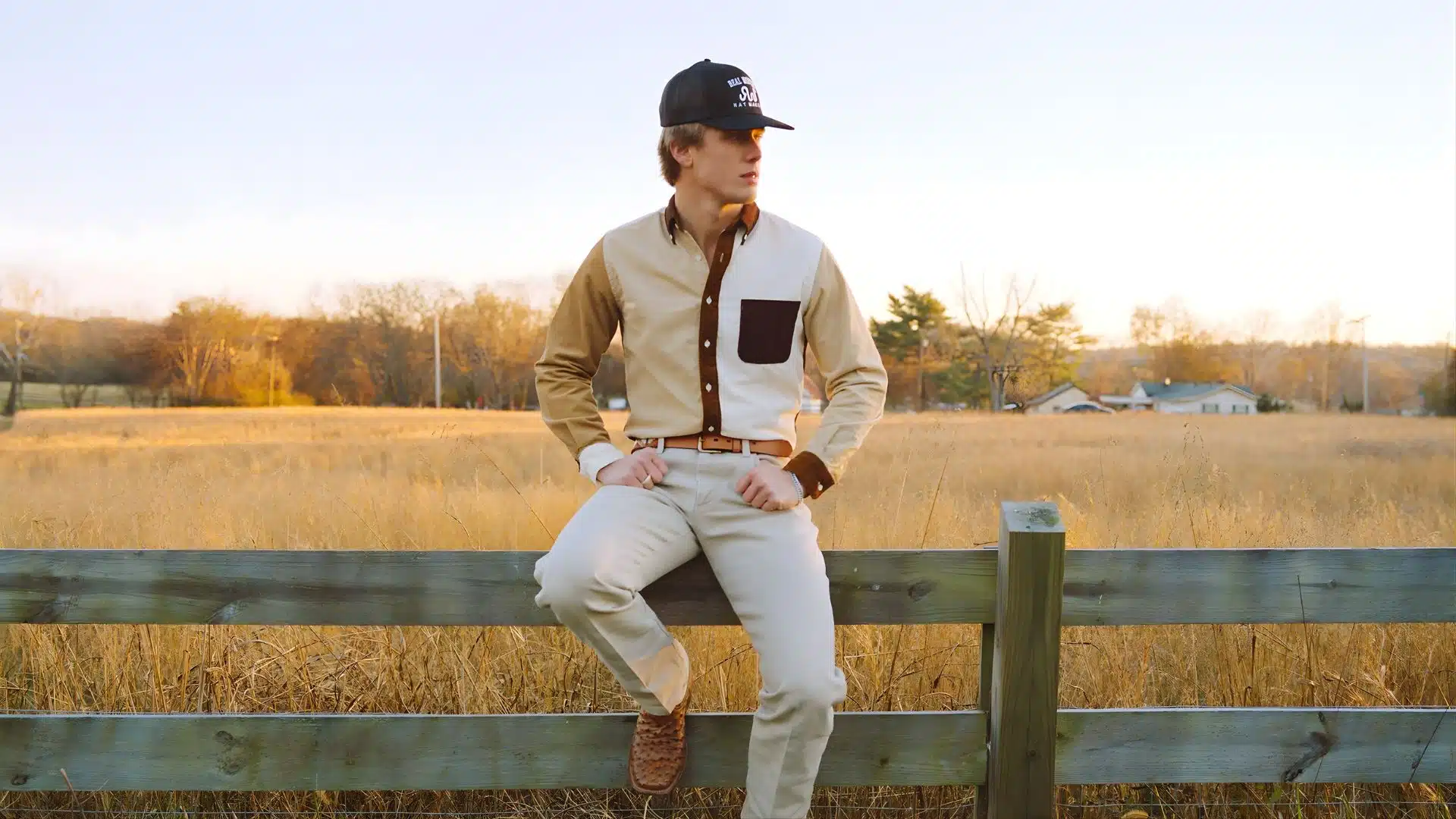 Hudson Westbrook sitting on a wooden fence in a field at sunset