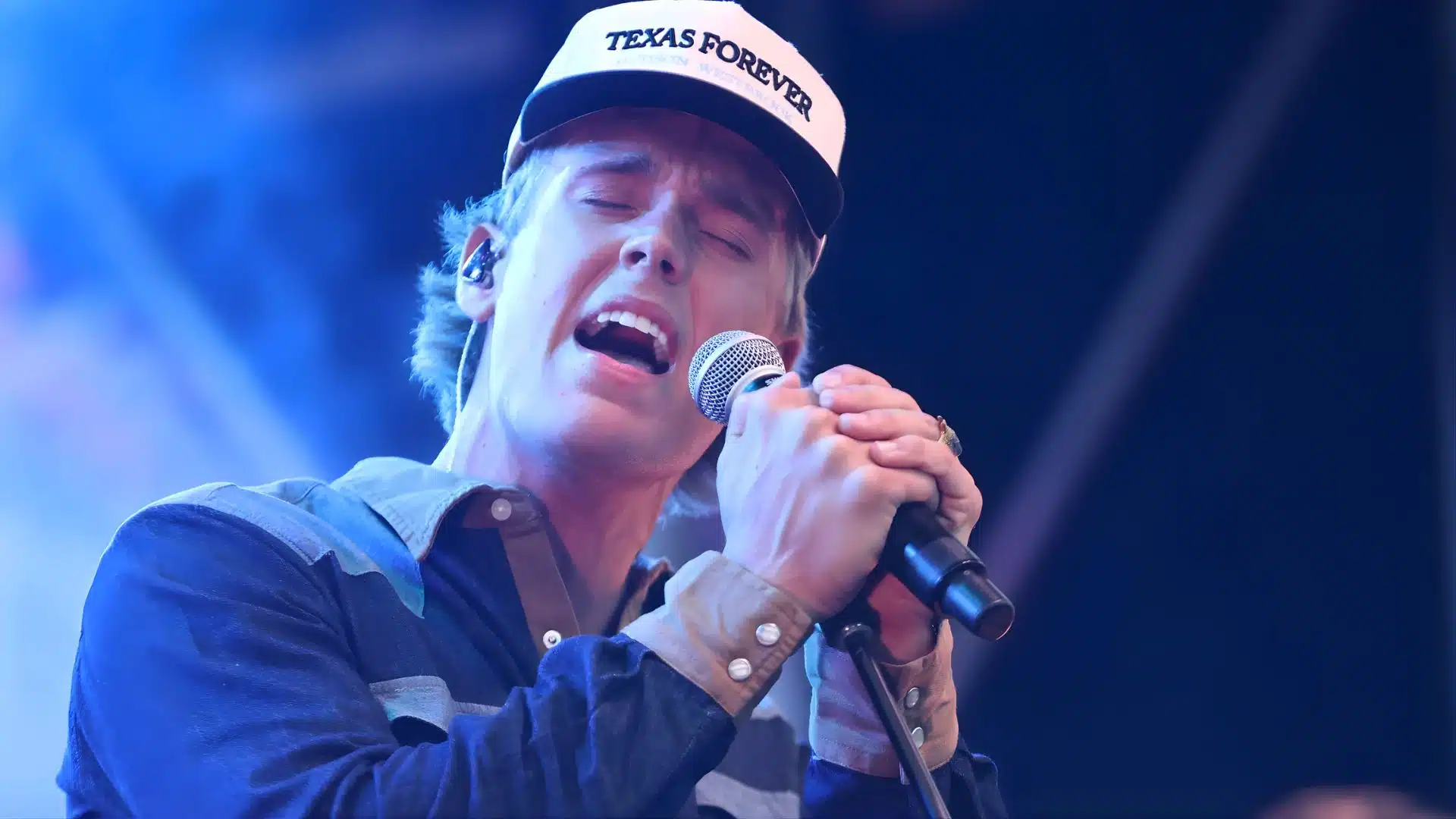 Hudson Westbrook singing into a microphone on stage, wearing a Texas Forever cap