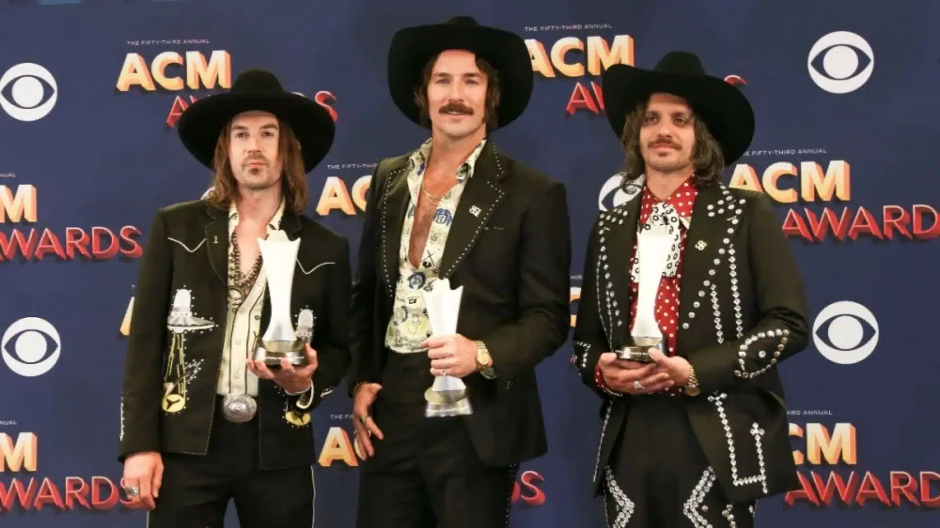 Midland band members holding their trophies in front of an ACM Awards backdrop.
