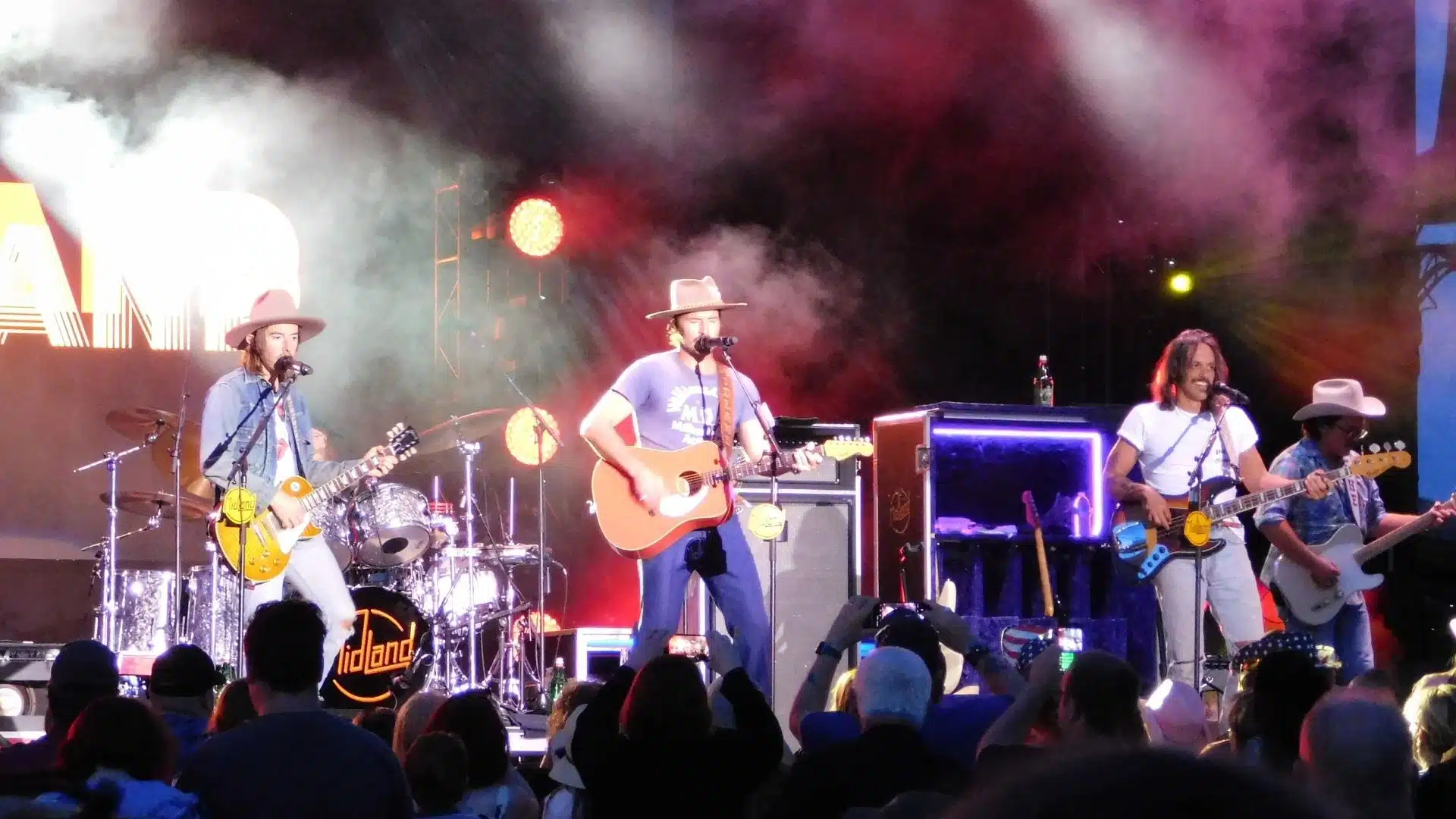 Midland performing live on stage with guitars and a drummer under bright concert lights.