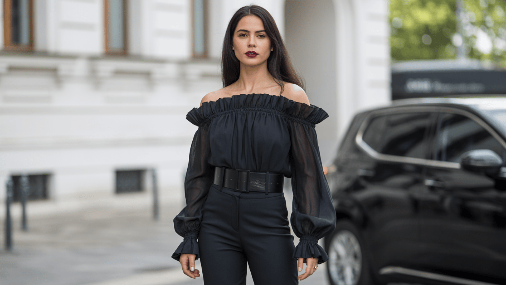 Off shoulder black blouse with sheer sleeves paired with high-waisted trousers in a city setting
