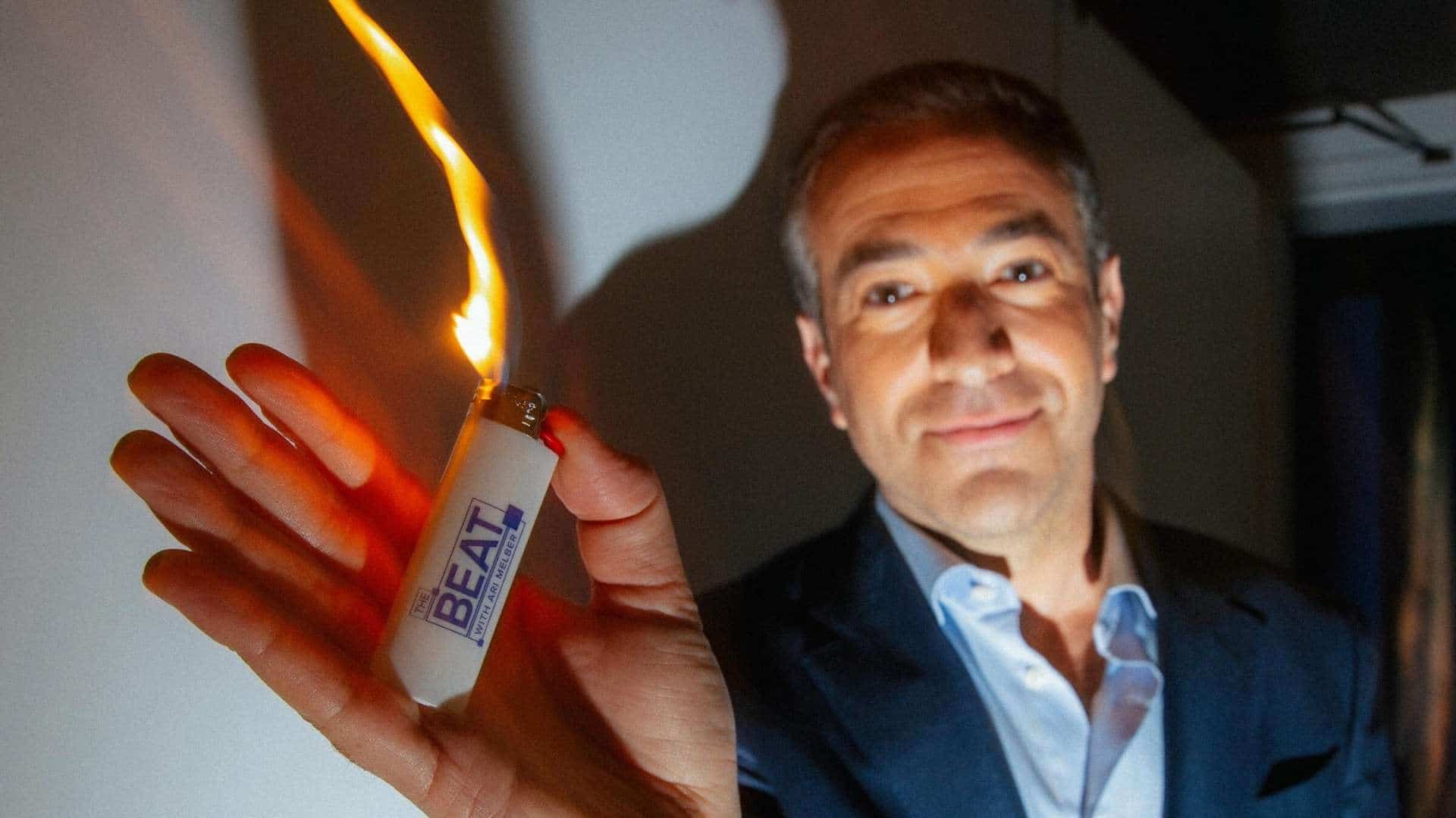 Ari melber holding a lit lighter with the beat branding while posing for a dramatic portrait