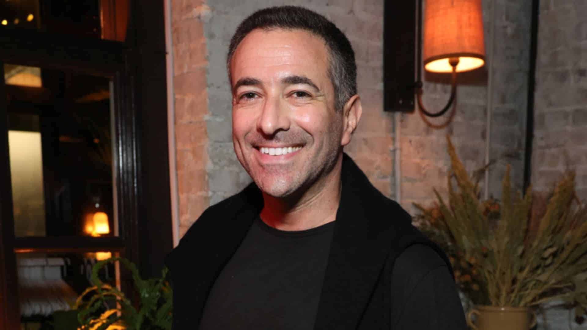 Ari melber smiling in a casual indoor setting with warm lighting