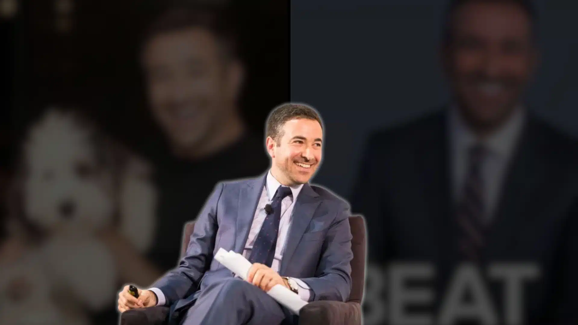 ari melber sitting on stage in a suit smiling during a public talk or event