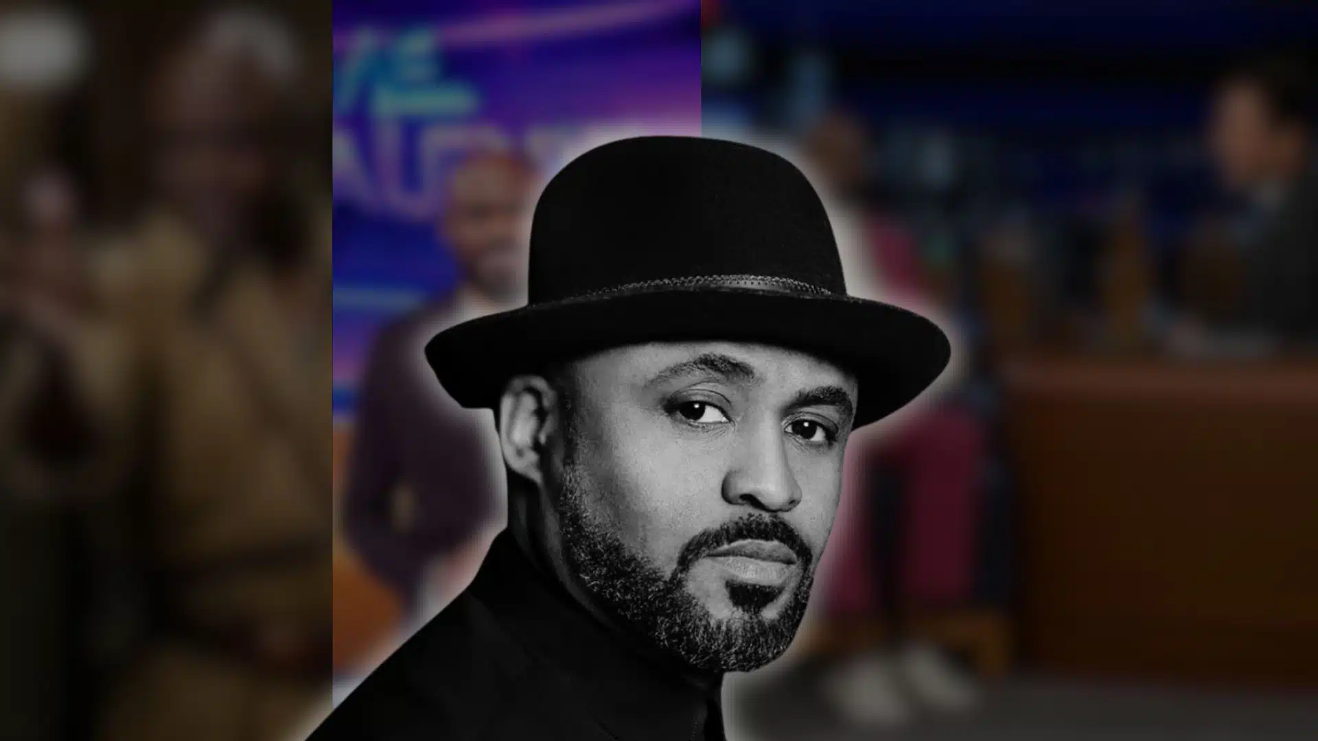 Close-up portrait of Wayne Brady wearing a black hat, with a blurred TV studio background