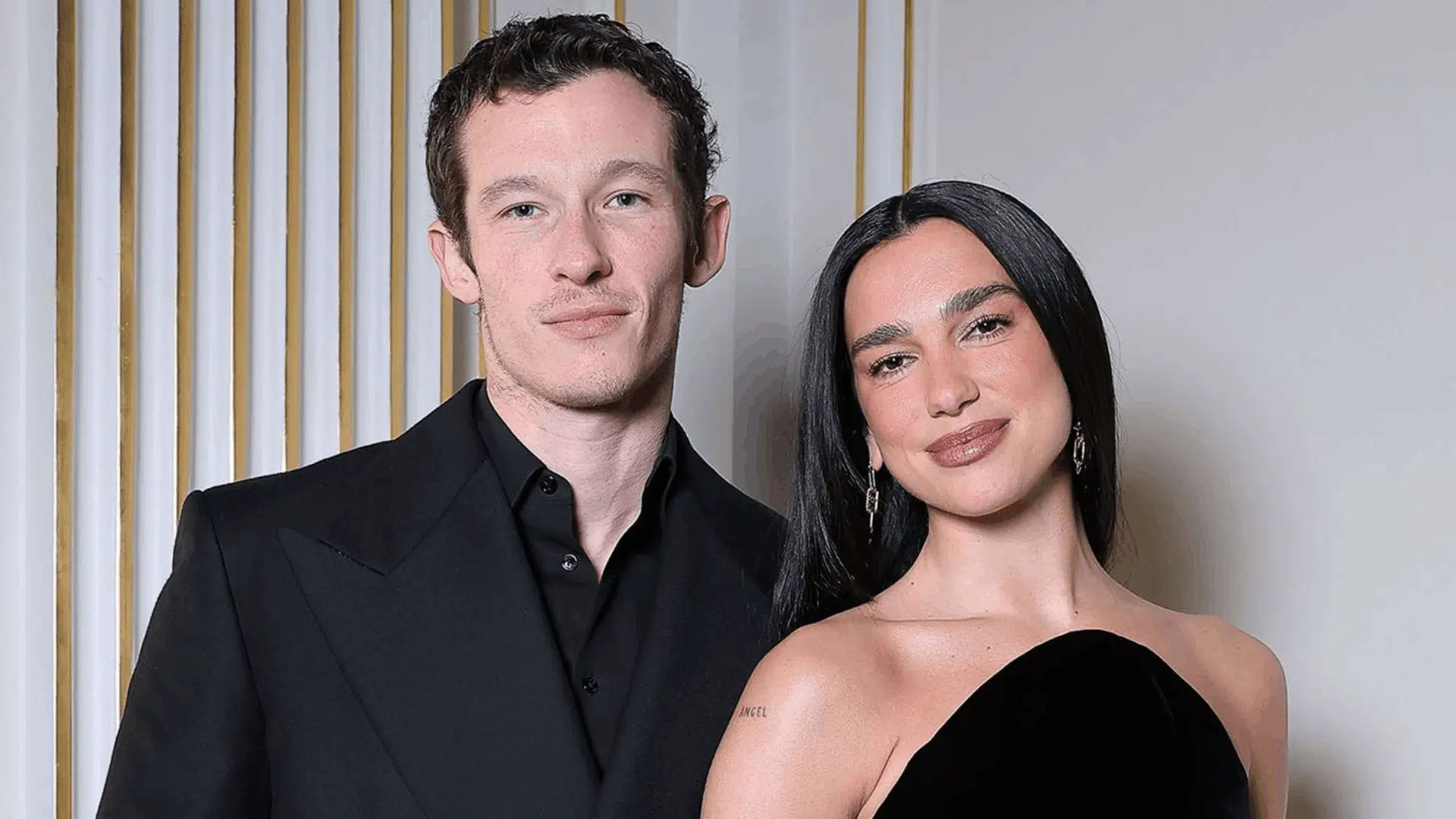 Dua Lipa and Callum Turner smiling together at a public event.