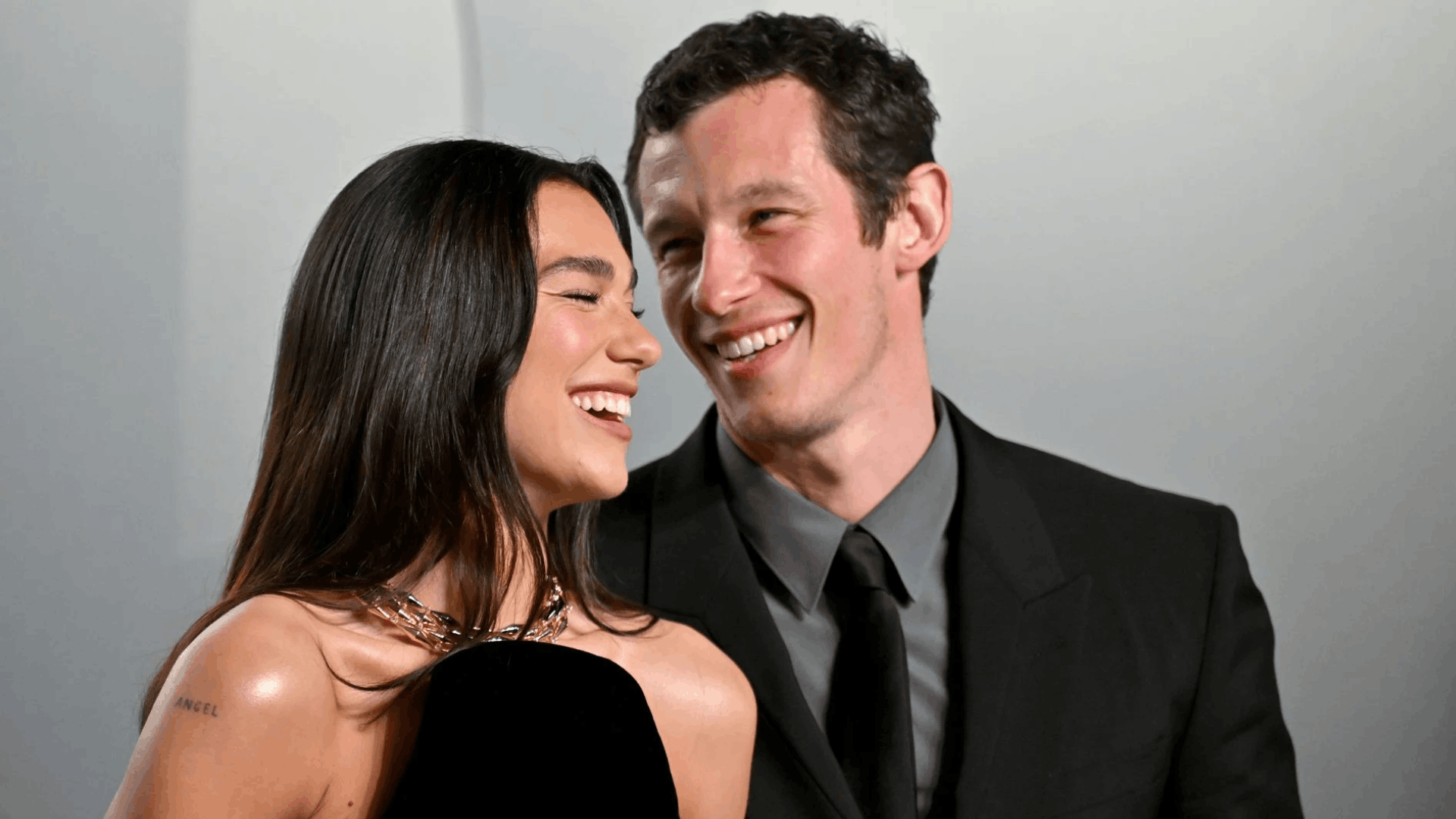 Dua Lipa and Callum Turner smiling together at a public event.