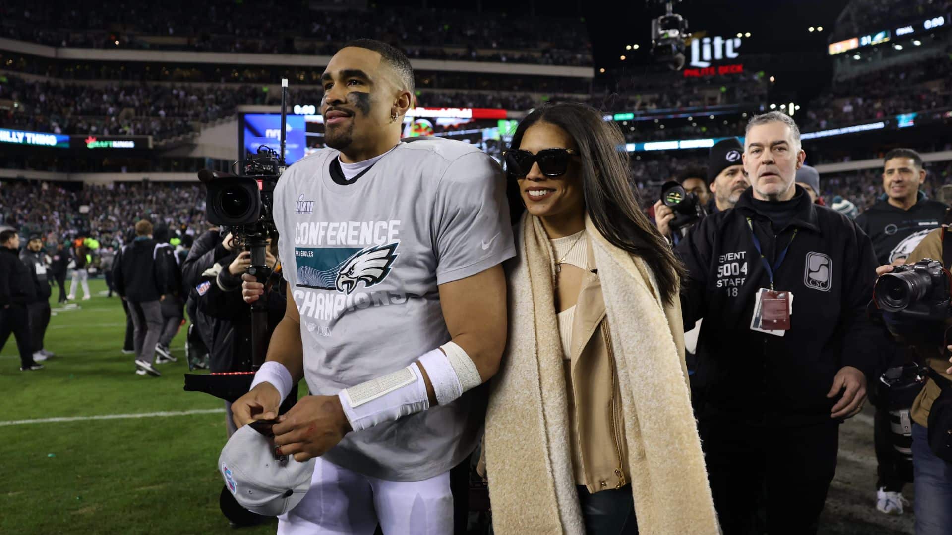 Jalen Hurts and Bry Burrows walk across the field after the Eagles' NFC Championship win, surrounded by media and fans.
