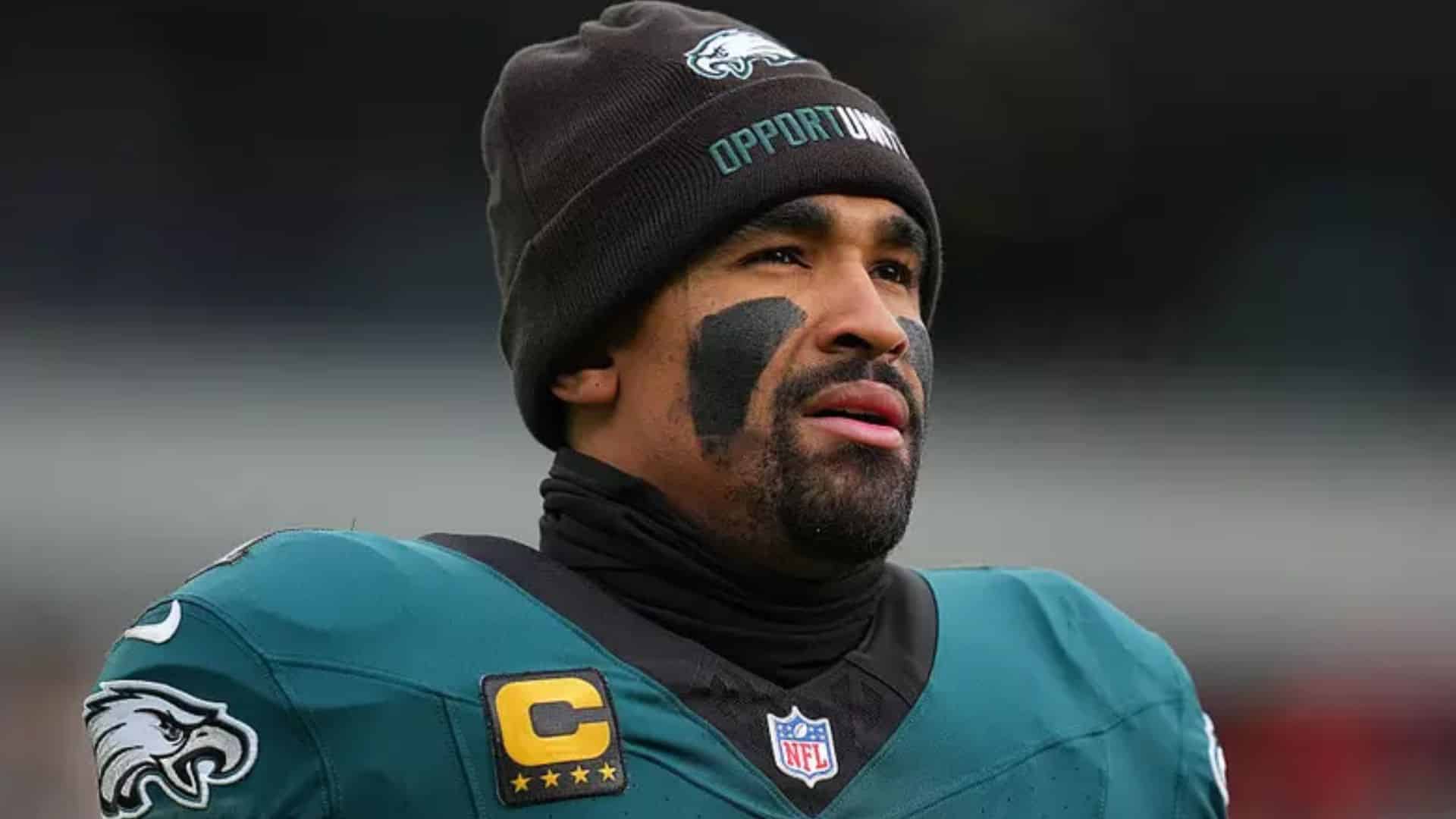 Jalen Hurts stands on the sideline in his Philadelphia Eagles uniform and beanie, looking toward the field before a game.