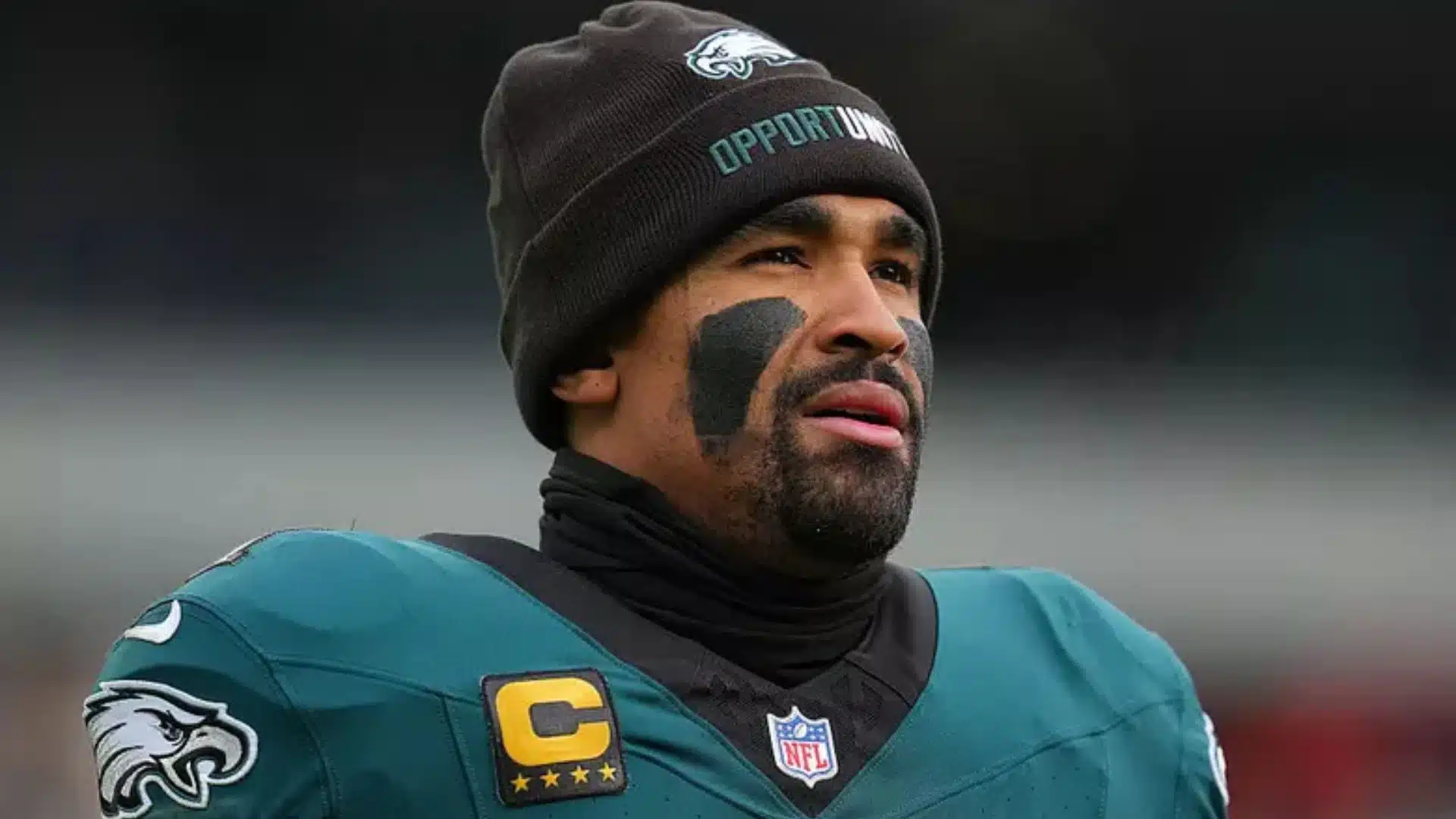 Jalen Hurts stands on the sideline in his Philadelphia Eagles uniform and beanie, looking toward the field before a game.
