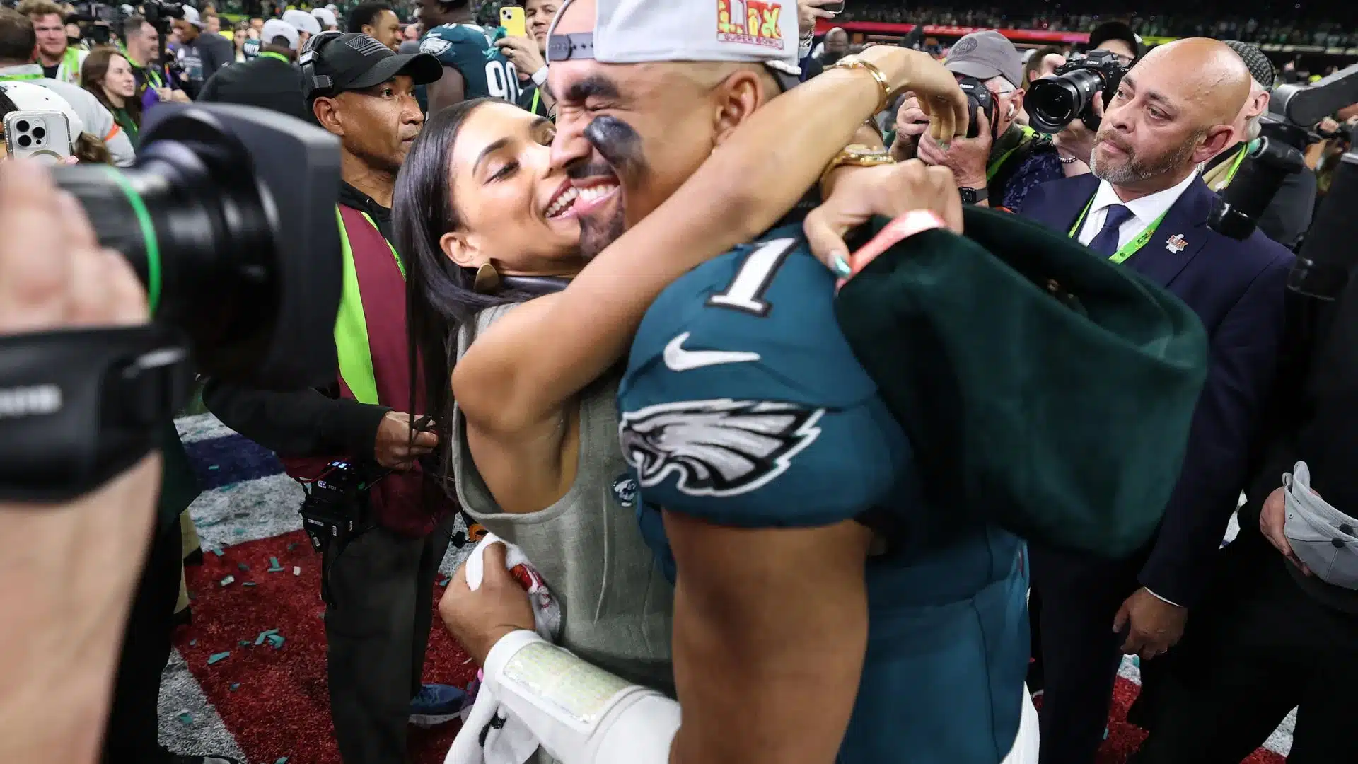 alen Hurts embraces Bry Burrows on the field after the Eagles' Super Bowl victory as photographers and team staff gather around them.
