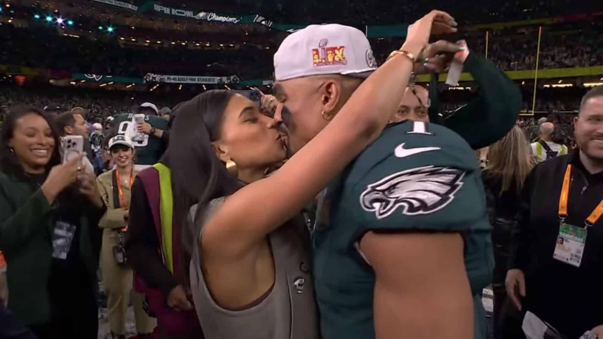 Bry Burrows kisses Jalen Hurts on the field as they celebrate the Eagles' Super Bowl victory surrounded by teammates, staff, and fans.