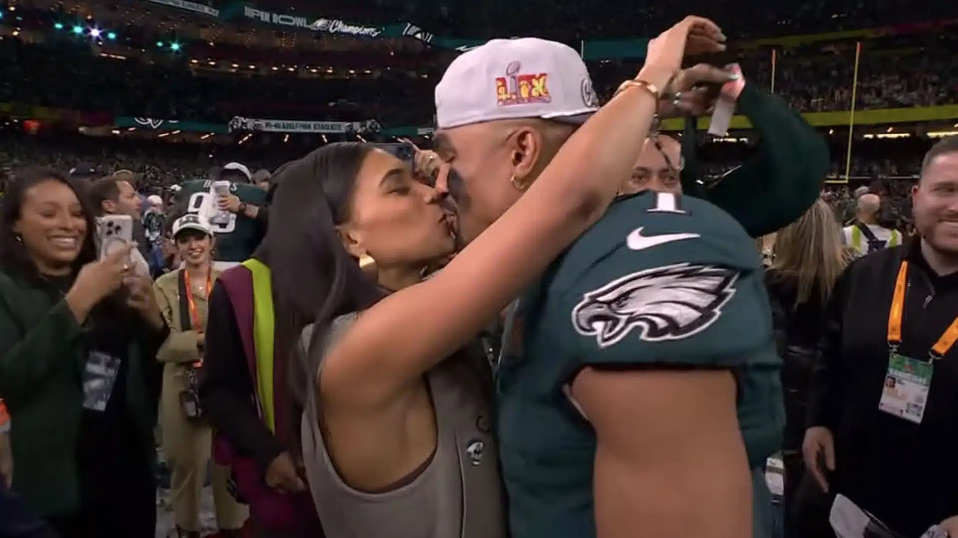 Bry Burrows kisses Jalen Hurts on the field as they celebrate the Eagles' Super Bowl victory surrounded by teammates, staff, and fans.