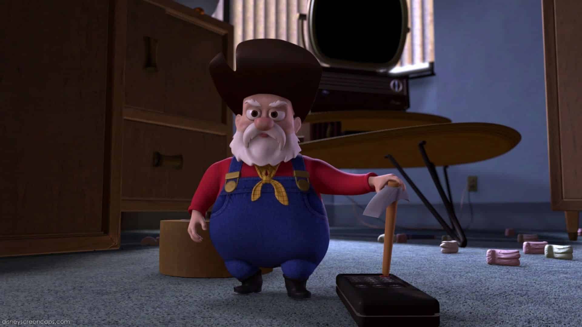 Stinky Pete the Prospector from Toy Story 2 standing with a stern expression while holding a TV remote.