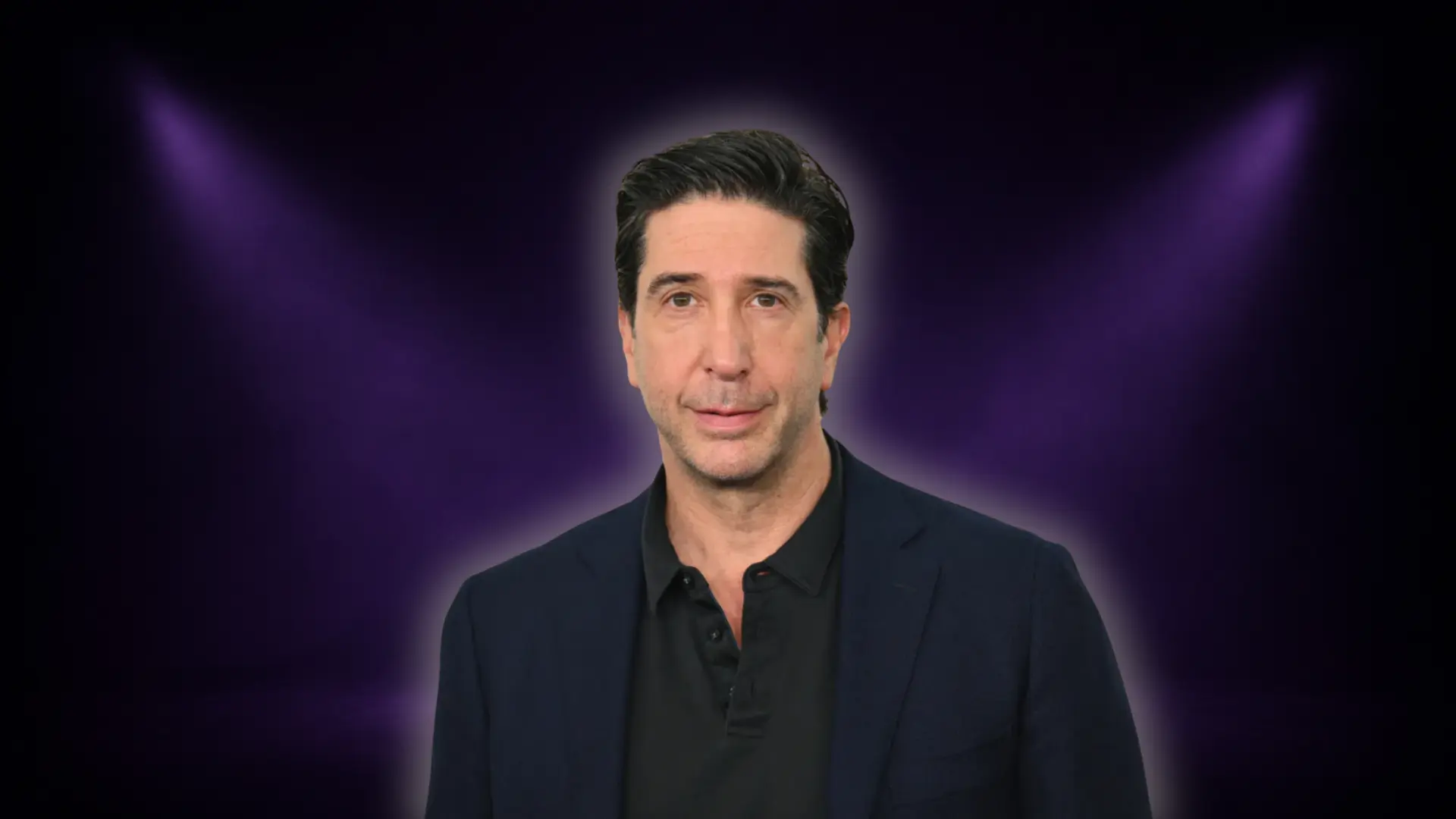David Schwimmer portrait on a dark purple stage-style background with soft spotlight glow behind him in a studio-style setup.