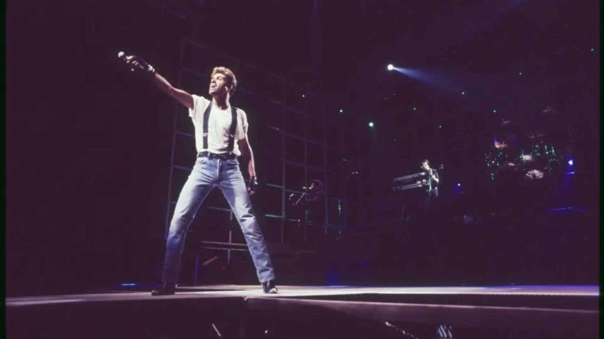 George Michael performing on stage during a concert with a microphone and stage lighting.