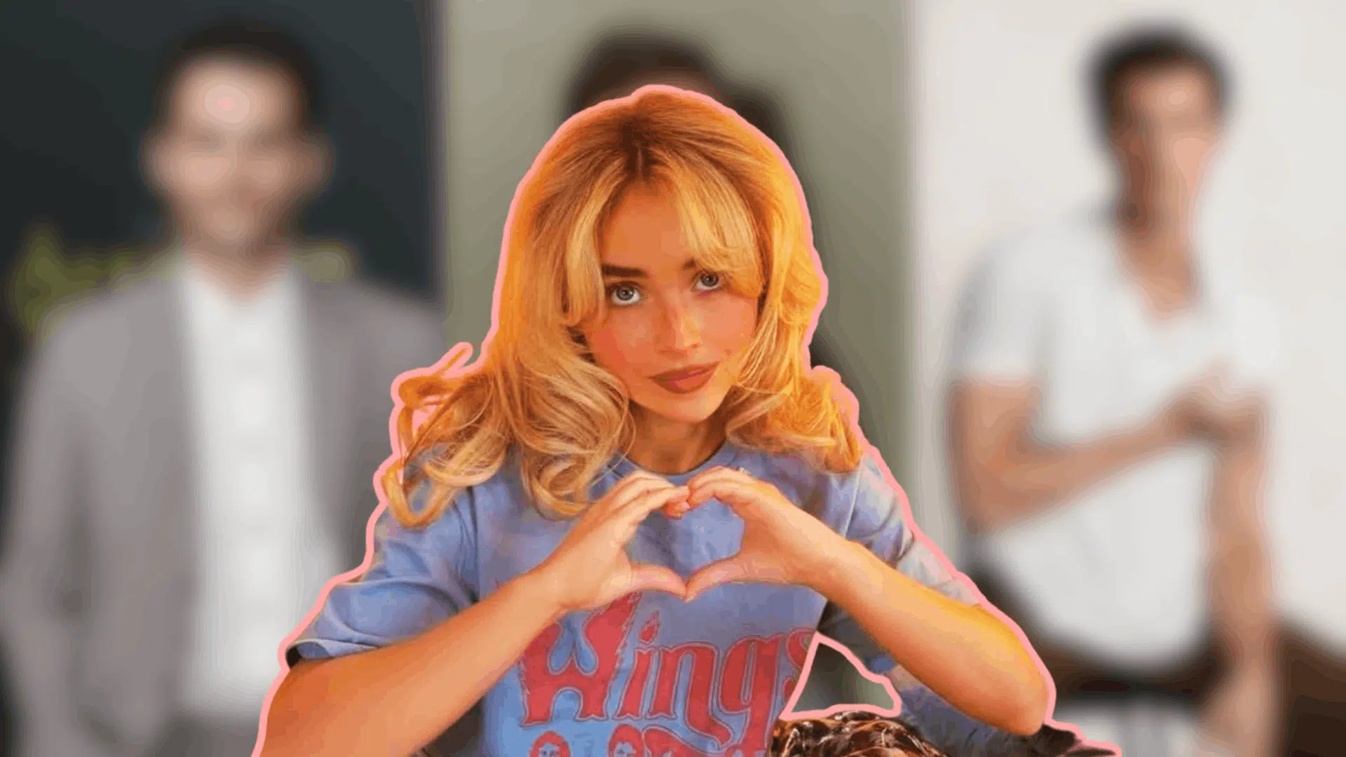 Sabrina Carpenter making heart hand gesture in foreground and blurred figures of possible partners in background.