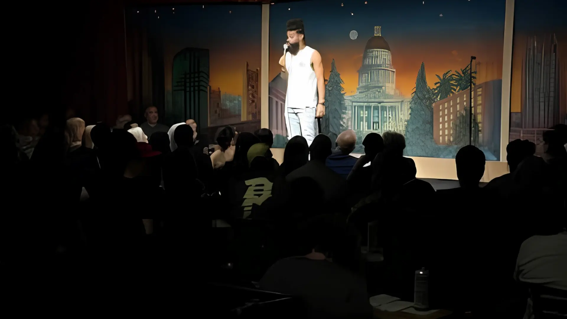 Damon Darling performing stand-up comedy on a theater stage in front of a full seated audience.